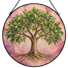 Load image into Gallery viewer, Rooted in Abundance Tree of Life stained glass-style suncatcher featuring lush green foliage, spreading roots, and a pink background with black metal frame and chain.