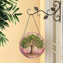 Load image into Gallery viewer, Rooted in Abundance Tree of Life glass suncatcher hanging from a decorative metal hook beside a sunlit window and leafy greenery.