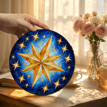 Ladda upp bild till gallerivisning, Hand displaying the Written in the Stars glass suncatcher near pink flowers, showcasing its golden stars and beautifully layered blue brushwork.