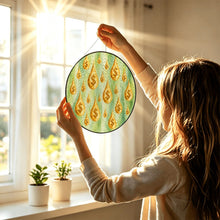 Load image into Gallery viewer, Woman holding the Make It Rain glass window hanging toward natural sunlight, showcasing golden dollar-sign raindrops on green artwork.
