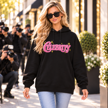 Carica l'immagine nel visualizzatore di Gallery, Blonde woman wearing a black Celebrity women's organic cotton blend side pocket hoodie with pink graphic, sunglasses and jeans on an upscale shopping street.