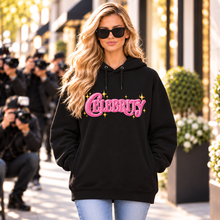 Carica l'immagine nel visualizzatore di Gallery, Blonde model in sunglasses wearing a black organic cotton blend hoodie featuring a pink Celebrity graphic while walking past photographers.