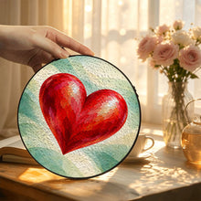 Load image into Gallery viewer, Hand displaying the Follow Your Heart glass suncatcher with vibrant red heart artwork near a sunlit window and pink flowers.