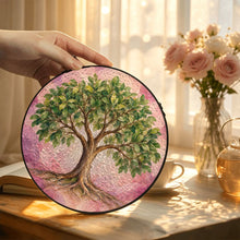 Load image into Gallery viewer, Hand displaying the Rooted in Abundance Tree of Life suncatcher, featuring green leaves and blush pink artwork beside a vase of flowers.