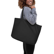 Cargar imagen en el visor de la galería, Model wearing a gray sweater carrying the Solar Pop oversized black organic cotton tote bag featuring original golden yellow and orange abstract circle artwork.