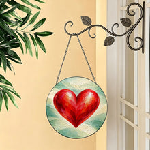Carica l'immagine nel visualizzatore di Gallery, Follow Your Heart red heart glass suncatcher hanging from a decorative metal hook beside a window with greenery.
