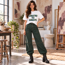 Carregar imagem no visualizador da galeria, Woman in a sunlit art studio wearing the Created to Create women’s organic t-shirt with green and blue Earth filled lettering.
