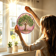 Carica l'immagine nel visualizzatore di Gallery, Woman holding the Rooted in Abundance Tree of Life glass suncatcher toward a sunny window, displaying its colorful tree artwork.
