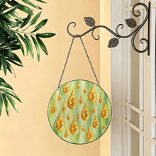 Carica l'immagine nel visualizzatore di Gallery, Make It Rain glass suncatcher with golden dollar-sign raindrops hanging from a decorative metal hook beside a window and greenery.
