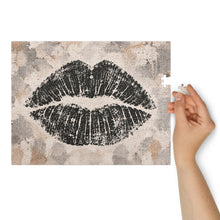 Load image into Gallery viewer, Lip Print jigsaw puzzle featuring an oversized black lip impression on a layered neutral cream, taupe, gray and stone background, from Little Yellow Bungalow.
