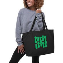 Cargar imagen en el visor de la galería, Model wearing a gray sweater carrying the Green Theory oversized black organic cotton tote bag, showcasing original electric green abstract artwork and spacious design.
